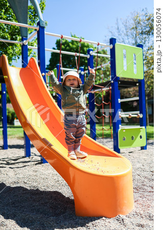 A Joyful Toddler Happily Climbing an Orange Slide at the Playground on a Beautiful Sunny Day, Full of Laughter and Excitement, Embracing the Freedom of Playtime Outdoors with Friends and Siblings 130056074