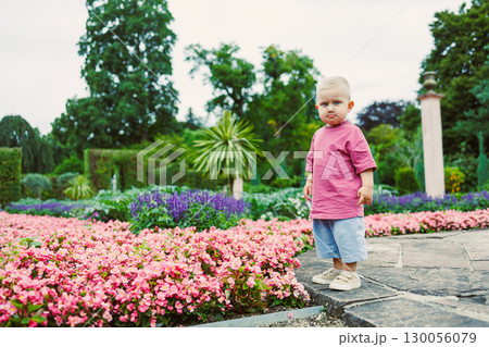 A charming toddler joyfully playing and exploring in a lush garden setting, surrounded by an array of colorful, blooming flowers that create a beautiful and vibrant outdoor environment 130056079