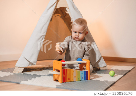 A playful baby is deeply engaged and having fun with a colorful musical toy while inside a cozy and comfortable tent, creating an enchanting environment filled with joy and creativity during playtime A playful baby is deeply engaged and having fun with a colorful musical toy while inside a cozy and comfortable tent, creating an enchanting environment filled with joy and creativity during playtime 130056176