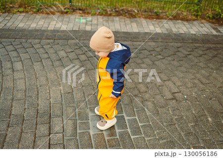 A cute and adorable child dressed in a bright yellow rain suit passionately exploring the great outdoors. Their innocent curiosity and joy radiate as they discover new things in the autumn landscape 130056186