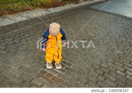 A joyful and playful young child, dressed in bright yellow rain gear, is happily exploring the great outdoors on a rainy day. This adventure highlights natural curiosity and childhood innocence 130056187