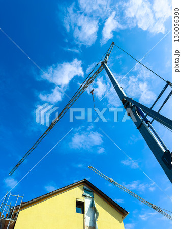 Construction Crane Against a Blue Sky with a Building Under Renovation Construction Crane Against a Blue Sky with a Building Under Renovation 130056390