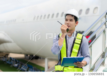 male engineer in a white hard hat stands inspecting and maintaining an aircraft as it moves through the hangar. 130056691
