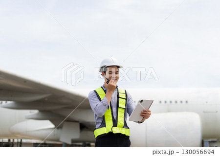 Male engineer in white hardhat standing and holding tablet working aircraft maintenance mechanics moving through hangar. 130056694