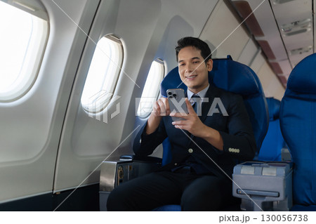 Waist up image of a fun businessman in an airline working on his computer while talking on a cell phone. 130056738