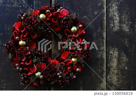 12月の背景イメージ、渋いブラウンの木製のドアに掛けられた赤い花と松ぼっくりのクリスマスリース 12月の背景イメージ、渋いブラウンの木製のドアに掛けられた赤い花と松ぼっくりのクリスマスリース 130056819