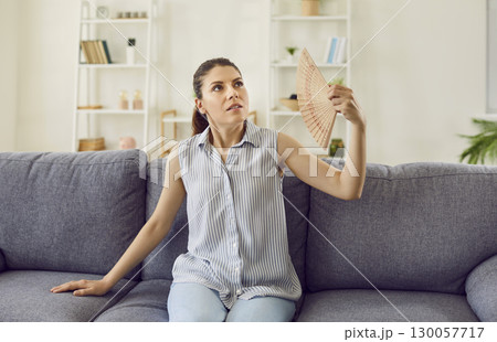 Stressed tired woman using fan suffering from heat, summer high temperature at home. 130057717