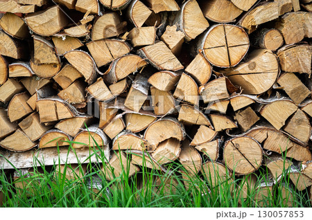 Woodpile of chopped firewood with green grass in front, stacked logs as a rustic background, natural fuel for winter heating, rural scene theme Woodpile of chopped firewood with green grass in front, stacked logs as a rustic background, natural fuel for winter heating, rural scene theme 130057853