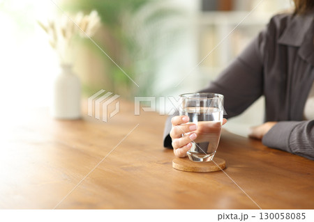 Woman hand holding water glass on wooden table Woman hand holding water glass on wooden table 130058085
