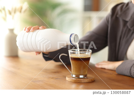 Woman hand pouring milk from bottle in coffee cup 130058087