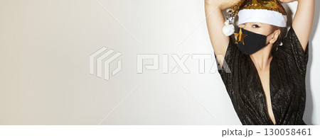 Woman with gold christmas hat, black medical mask. Fashion shiny style for xmas time. Protection from flu on holidays 130058461