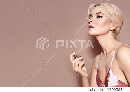 Beautiful Woman Applying Perfume Spray on neck. Blond Model with sexy Retro Make-up in Pink Lingerie Smells Fragrance 130058544