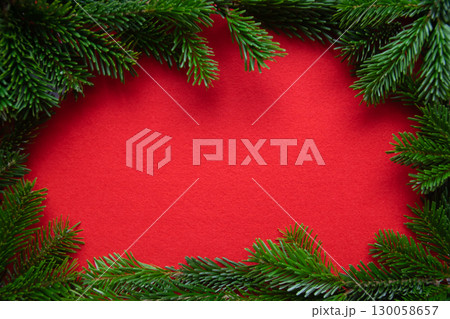 Red bright Christmas background. Winter frame of green branch on the textured fabric background. Red bright Christmas background. Winter frame of green branch on the textured fabric background. 130058657