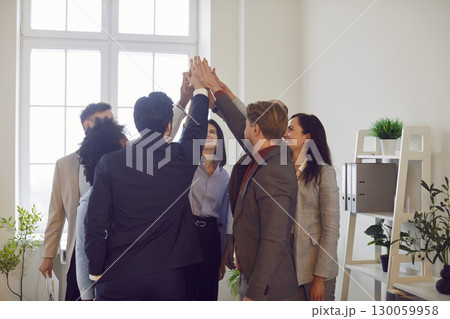 Happy diverse business team standing in circle, stacking hands, symbolizing unity and shared goals. Happy diverse business team standing in circle, stacking hands, symbolizing unity and shared goals. 130059958