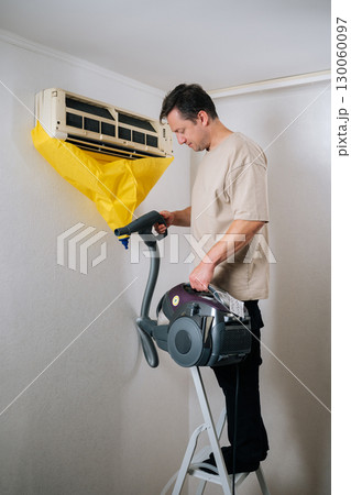 Vertical shot of technician standing on ladder, cleaning air conditioner unit with vacuum cleaner while using yellow plastic bag to collect dust and dirt for effective maintenance and hygiene Vertical shot of technician standing on ladder, cleaning air conditioner unit with vacuum cleaner while using yellow plastic bag to collect dust and dirt for effective maintenance and hygiene 130060097