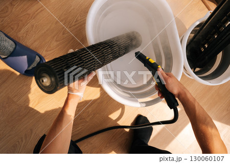 Top view of unrecognizable cleaning service employee washing air conditioner filter with steam cleaner, focusing on maintenance and cleaning tasks, ensuring thorough hygiene 130060107