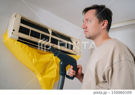 HVAC professional standing on ladder, vacuuming air conditioning unit, collecting debris in yellow plastic bag during routine maintenance service. Concept of air condition hygiene. 130060109
