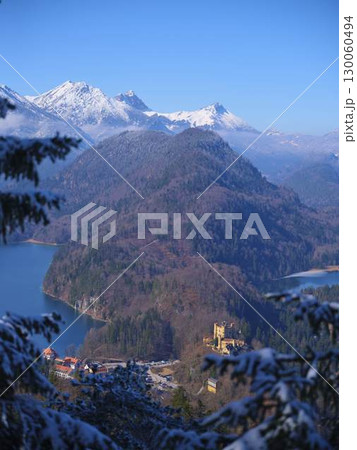 Snow-covered mountains surround a historic castle near a serene lake during a clear winter day Snow-covered mountains surround a historic castle near a serene lake during a clear winter day 130060494