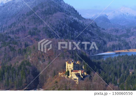 Beautiful castle nestled in the mountains near a serene lake under clear blue skies Beautiful castle nestled in the mountains near a serene lake under clear blue skies 130060550