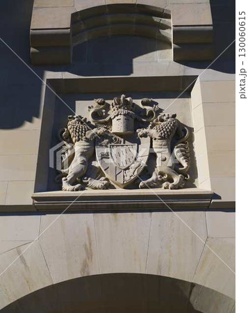 Historic stone emblem featuring lions and a shield displayed on a building facade in bright sunlight 130060615