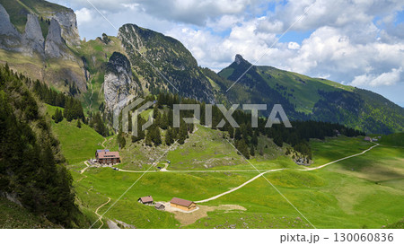 Mountain landscape features lush greenery and rocky cliffs with charming cabins under a bright sky 130060836