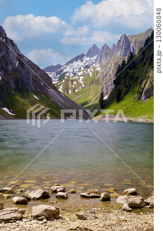 Stunning alpine lake surrounded by mountains in the summer with clear blue skies and lush greenery 130060848