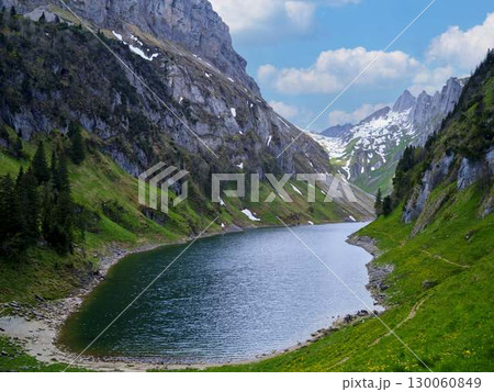 Scenic mountain landscape with a tranquil lake surrounded by lush greenery and snow-capped peaks 130060849