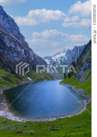 Serene mountain lake surrounded by lush greenery and towering peaks on a clear day 130060850