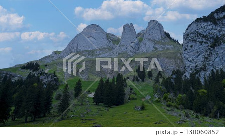 Scenic mountain landscape with towering peaks and lush greenery under a blue sky filled with fluffy clouds 130060852