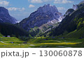 Majestic mountains rise above a lush valley with scattered farmhouses in a picturesque landscape under blue skies 130060878