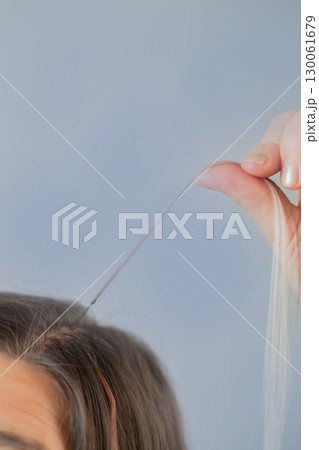 Woman holding hair strand with capsule before applying professional hair extension technique in beauty salon 130061679