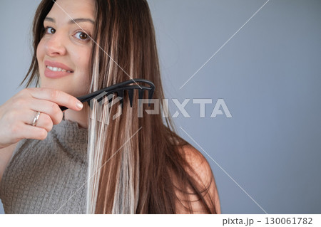 Woman caring for hair extensions using wide tooth comb showing ease and gentle hair maintenance in salon Woman caring for hair extensions using wide tooth comb showing ease and gentle hair maintenance in salon 130061782