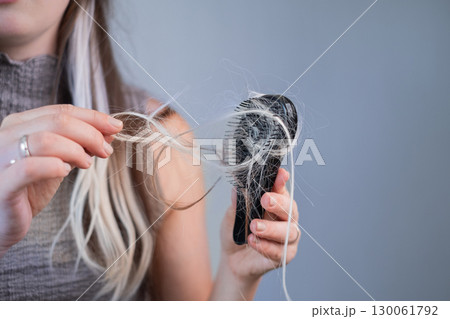 Woman with brittle hair holding hairbrush with fallen strands showing hair loss and breakage problem 130061792