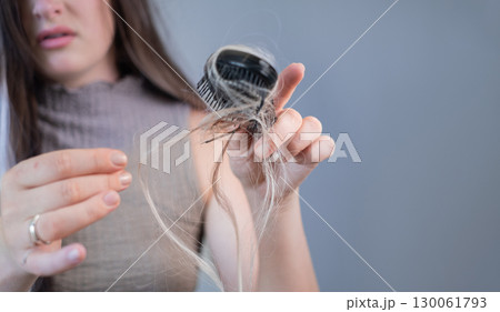 Sad young woman noticing broken strands on hairbrush showing hair thinning and early signs of hair loss 130061793