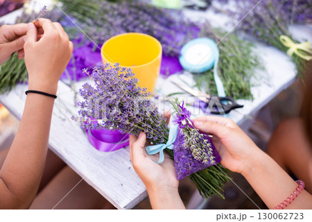Lavender bouquet and sachet in hands of a girl sitting near the table, close up. Preparing natural beauty, aromatherapy, beautiful and scented plant 130062723