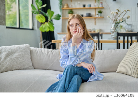 Sad unhappy upset young woman sitting at home on sofa, face close-up 130064109