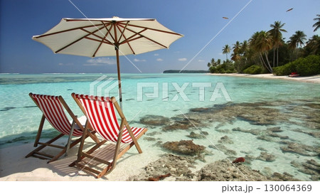 Scenic tropical beach with two colorful striped deck chairs under a large parasol 130064369