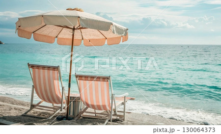 Scenic tropical beach with two colorful striped deck chairs under a large parasol 130064373
