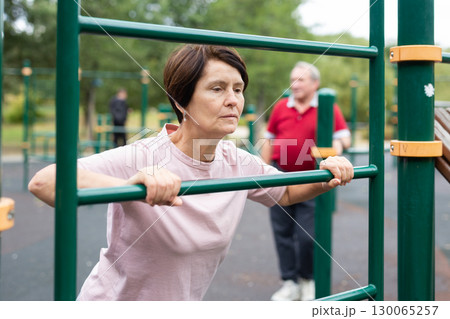 elderly woman doing exercises on a horizontal bar at an outdoor sports ground elderly woman doing exercises on a horizontal bar at an outdoor sports ground 130065257