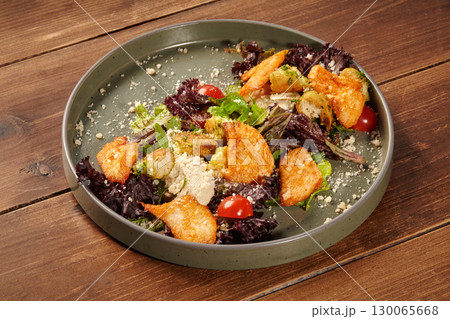 Delicious caesar salad with chicken, croutons, parmesan, and cherry tomatoes on rustic wooden table 130065668