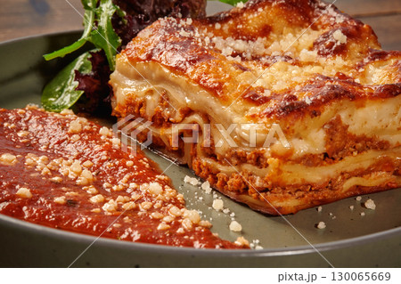 Delicious lasagna bolognese with grated parmesan and arugula on rustic plate 130065669