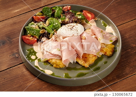 Potato pancakes with ham, poached egg and salad on wooden table Potato pancakes with ham, poached egg and salad on wooden table 130065672