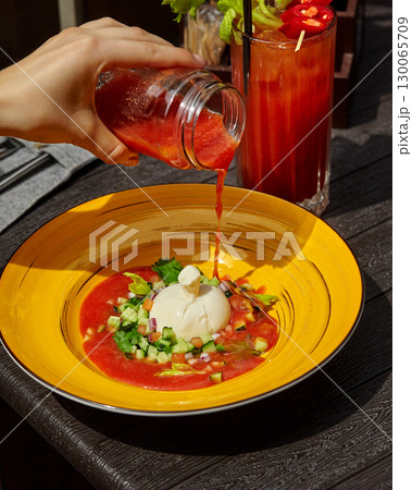Chef pouring gazpacho over burrata cheese and chopped vegetables 130065709