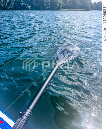 Close-up of a paddle over blue rippling lake water with forest in the background, symbolizing adventure, kayaking, and outdoor activities. High quality photo 130066214