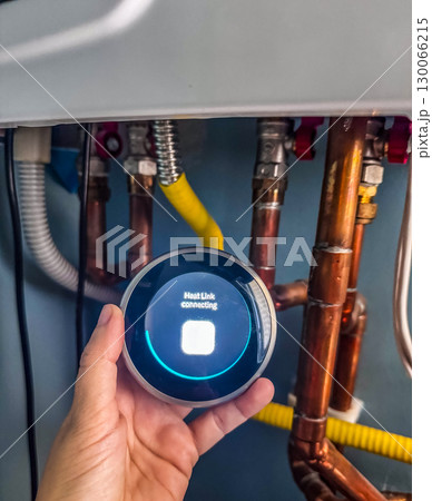 Hand holding a smart thermostat device attempting to connect to heating system pipes High quality photo 130066215