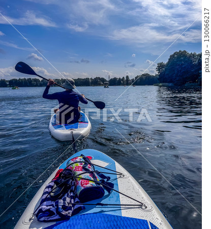 Person enjoying paddle boarding on a bright summer day with calm water and scenic forest view. High quality photo 130066217