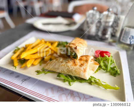 A plate with french fries and a vegetable wrap is served on a table. Casual dining, fast food and restaurant lifestyle. 130066812