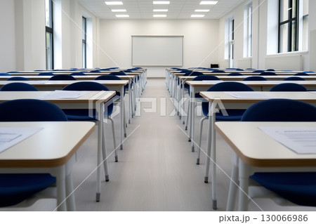 Modern classroom interior with rows of empty desks and blue chairs, facing a whiteboard. 130066986
