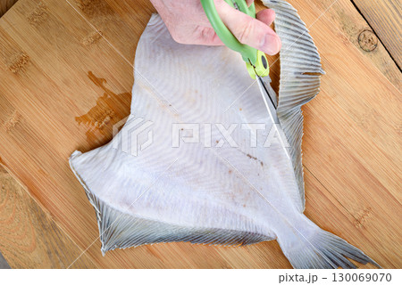 Cutting off the fins of flounder fish with kitchen scissors before cooking. 130069070