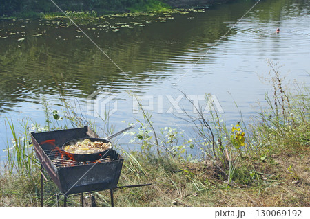 Cooking fried mussels in frying pan. Frying fresh mussels and onions near river 130069192